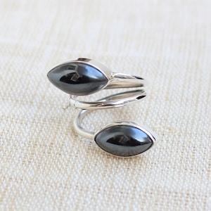 May include: A silver ring with two black oval-shaped stones. The ring is designed with a twisted band.
