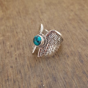 Op de afbeelding: Zilveren ring met een turquoise steen in het midden, gevormd als een paar vleugels.