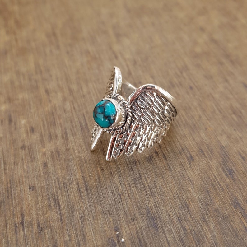 Op de afbeelding: Zilveren ring met een turquoise steen in het midden, gevormd als een paar vleugels.