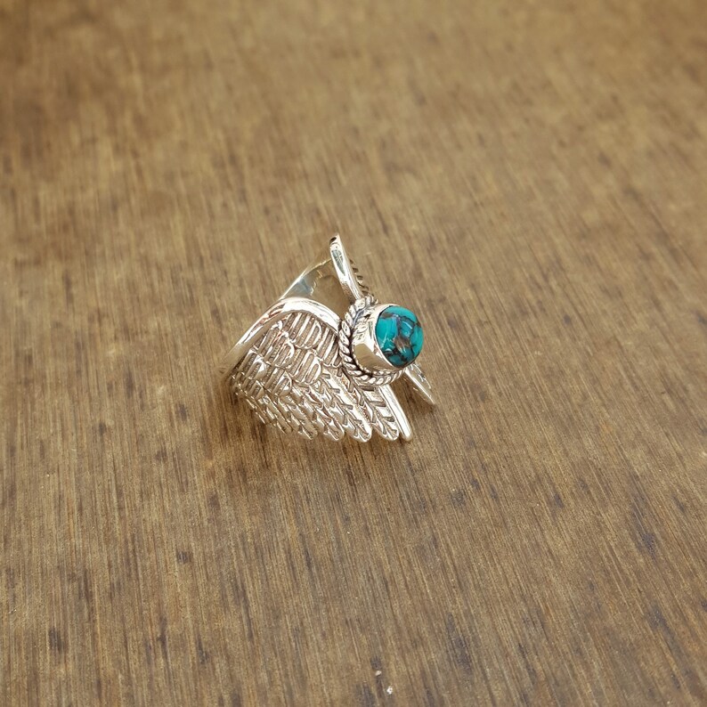 Op de afbeelding: Zilveren ring met een turquoise steen in het midden, gevormd als vleugels.