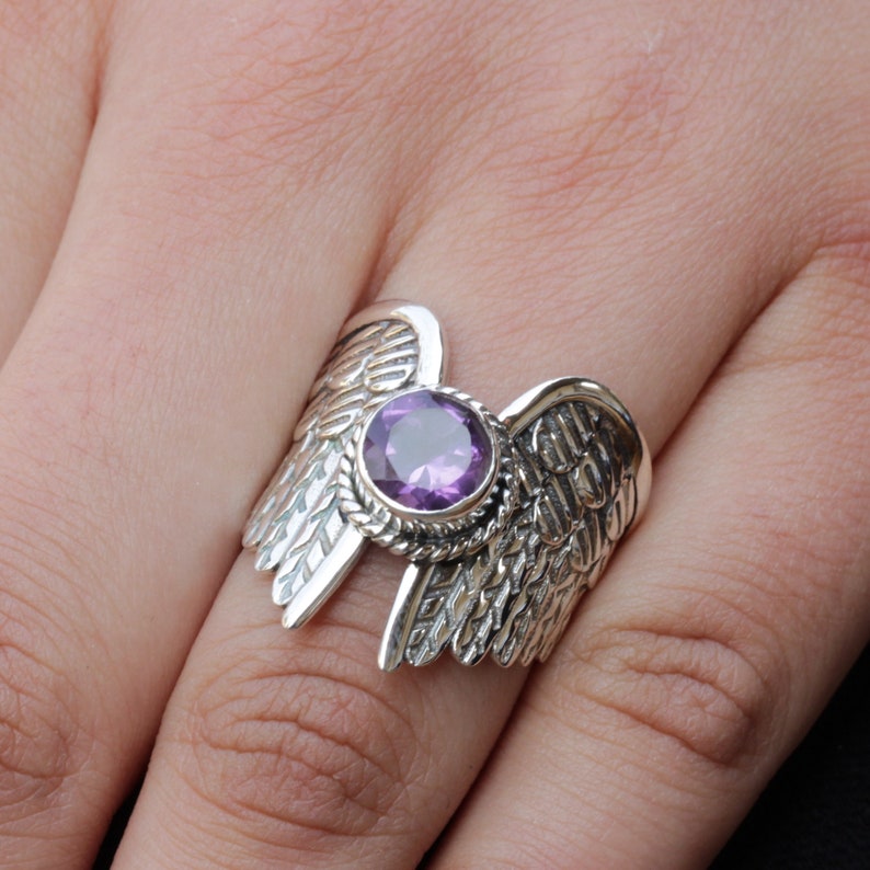 May include: A silver ring with a purple gemstone set in the center, surrounded by detailed wing designs.