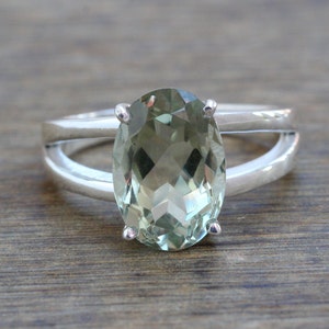 May include: A silver ring with a large oval green gemstone. The ring has a split band design.