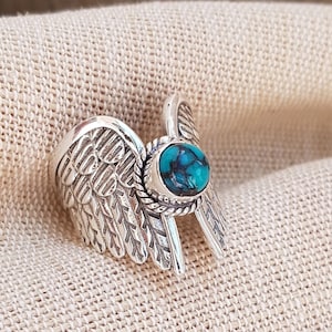 Op de afbeelding: Zilveren ring met een turquoise steen in een gedetailleerd vleugelontwerp.