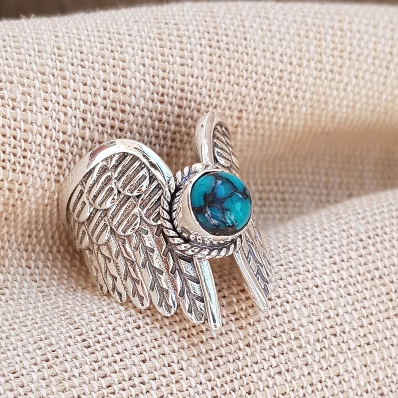 Op de afbeelding: Zilveren ring met een turquoise steen in een gedetailleerd vleugelontwerp.