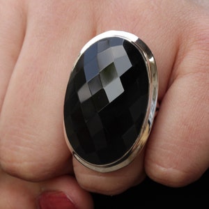 May include: A silver ring with a large, faceted black onyx stone. The stone is oval shaped and has a high polish.