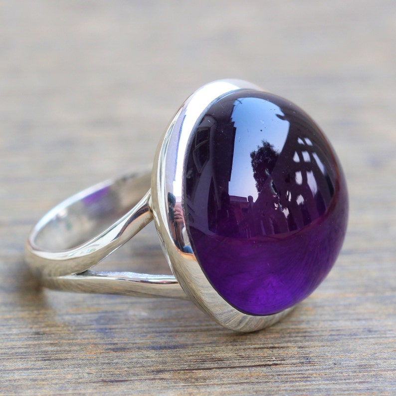 May include: A silver ring with a large, oval-shaped amethyst gemstone. The gemstone is a deep purple color and has a high polish.