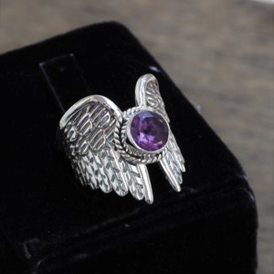 May include: A silver ring with a purple amethyst gemstone set in a wing design.