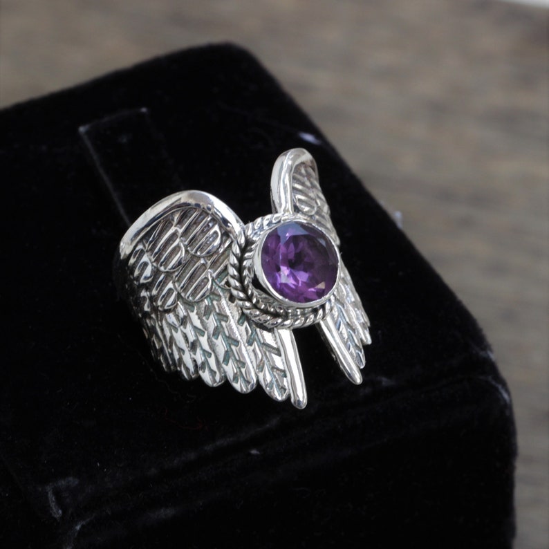 May include: A silver ring with a purple amethyst gemstone set in a wing design.