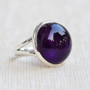 May include: A silver ring with a large, round, deep purple amethyst gemstone.