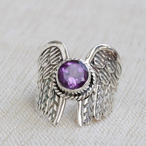 May include: A silver ring with a purple gemstone set in a detailed wing design.