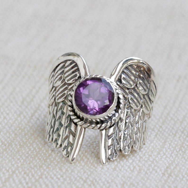 May include: A silver ring with a purple gemstone set in a detailed wing design.