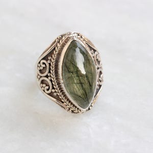 K&ouml;nnte beinhalten: Ein silberner Ring mit einem verzierten Design und einem gro&szlig;en, gr&uuml;nen, marmorierten Edelstein.