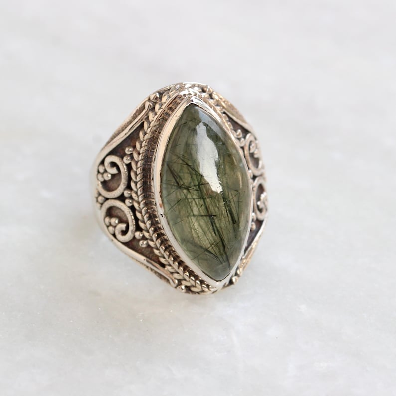K&ouml;nnte beinhalten: Ein silberner Ring mit einem verzierten Design und einem gro&szlig;en, gr&uuml;nen, marmorierten Edelstein.