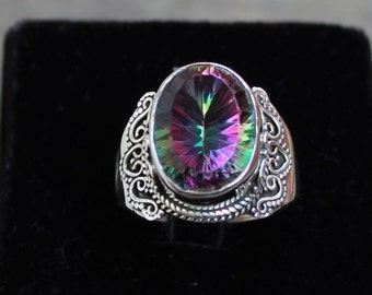Può includere: Anello in argento con una pietra preziosa ovale e iridescente. La pietra mostra uno spettro di colori che include viola, verde e giallo. L'anello presenta un design a filigrana ornato sulla fascia, che gli conferisce un aspetto vintage.