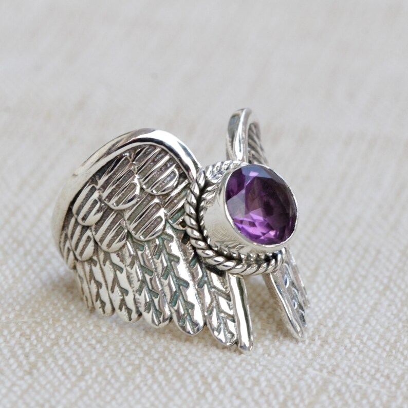 May include: A silver ring with a purple gemstone set in a wing design.