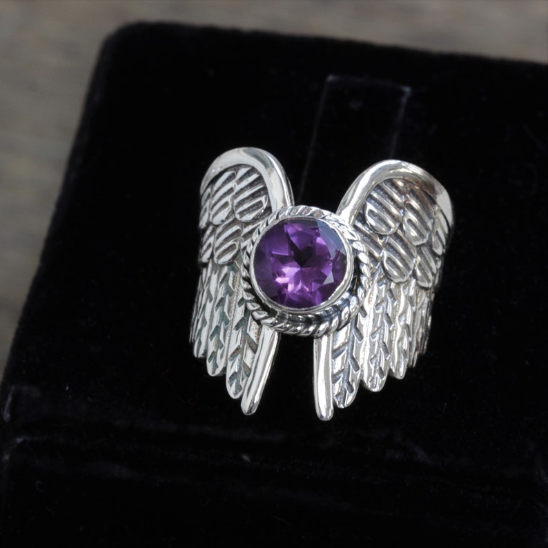 May include: A silver ring with a purple gemstone set in a detailed wing design.