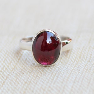 May include: A silver ring with a deep red oval gemstone.