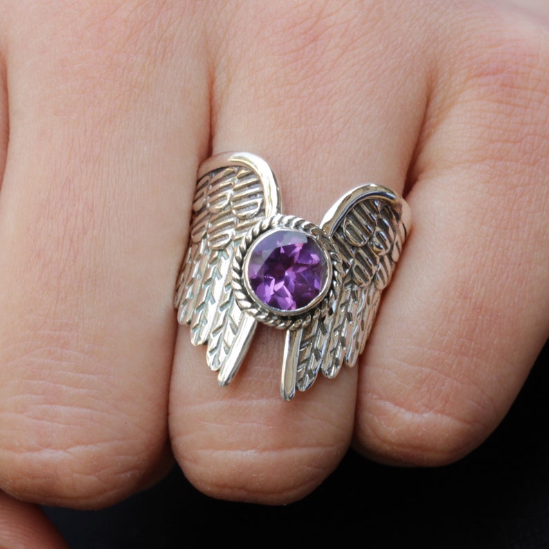 May include: A silver ring with a purple gemstone set in the center, surrounded by detailed wings.