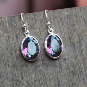 May include: A pair of silver dangle earrings with oval-shaped iridescent gemstones. The gemstones have a mix of green, purple, and pink hues.