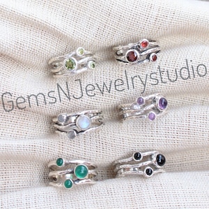May include: Six silver rings featuring different coloured gemstones. Each ring has three bands with a gemstone on each band. The gemstones are green, red, white, purple, black, and green.