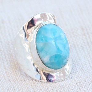 May include: A silver ring with a large, oval-shaped blue and white gemstone. The ring has a textured, hammered band.