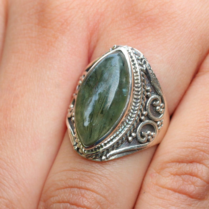 K&ouml;nnte beinhalten: Ein silberner Ring mit einem gro&szlig;en, gr&uuml;nen, marmorierten Edelstein, der in einem detaillierten, verzierten Design gefasst ist.