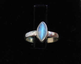 May include: A silver ring featuring a marquise-shaped moonstone. The stone displays a blue iridescent sheen.