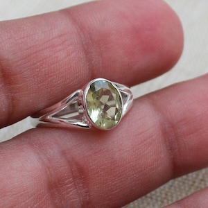 May include: A silver ring with a light green oval gemstone. The ring has a delicate, openwork design.