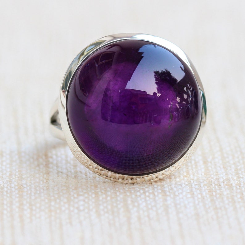 May include: A silver ring with a large, round, purple amethyst gemstone.