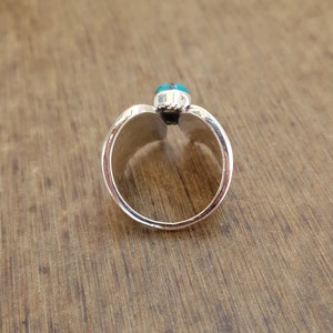 Op de afbeelding: Een zilveren ring met een turquoise steen in het midden. De ring is open en heeft een gespleten band.