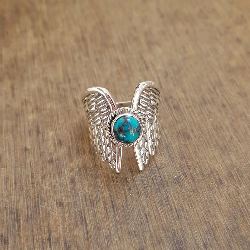 Op de afbeelding: Zilveren ring met een turquoise steen in het midden, gevormd als vleugels.