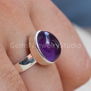 May include: A silver ring with a large, oval-shaped amethyst gemstone. The gemstone is a deep purple color and has a smooth, polished finish.