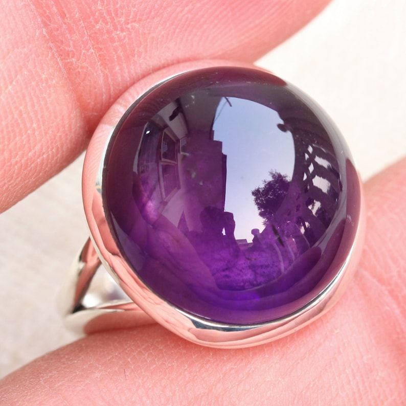 May include: A silver ring with a large, round, purple amethyst gemstone.