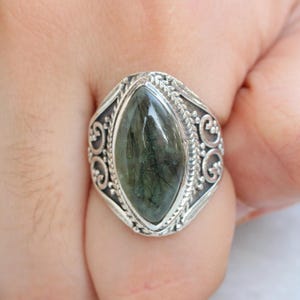 K&ouml;nnte beinhalten: Ein silberner Ring mit einem verzierten Design zeigt einen gro&szlig;en, dunkelgr&uuml;nen Edelstein mit einem marmorierten Muster.