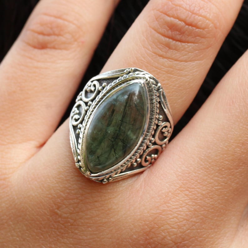 K&ouml;nnte beinhalten: Ein silberner Ring mit einem verzierten Design, das einen gr&uuml;nen Edelstein in der Mitte zeigt.