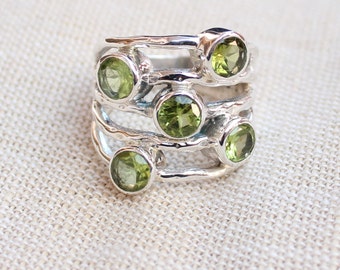 May include: A silver ring with five green gemstones set in a textured band. The ring has a unique, organic design.