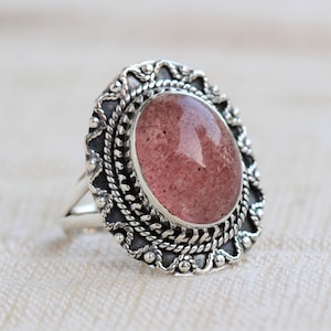 Peut inclure: Une bague en argent avec une pierre précieuse rose sertie dans un motif orné détaillé.
