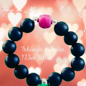 Könnte beinhalten: Ein schwarzes Perlenarmband mit einem rosafarbenen Stein und silbernen Akzenten. Das Armband ist aus Schungit gefertigt und trägt den Text "Schungit / Rubin 925er Silber".
