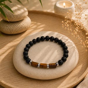 Peut inclure: Un bracelet composé de perles rondes en pierre de lave noire poreuse et de trois perles cylindriques en œil-de-tigre marron. Les perles en œil-de-tigre sont séparées par de petites entretoises métalliques argentées, créant un contraste entre la lave texturée sombre et les segments de pierre brune polis.