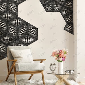 May include: A white armchair with a wooden frame and a white pillow sits on a fluffy white rug in front of a white wall with a black and white geometric design. A glass coffee table with a wooden base sits in front of the chair. A vase with pink flowers and a silver alarm clock are on the table.