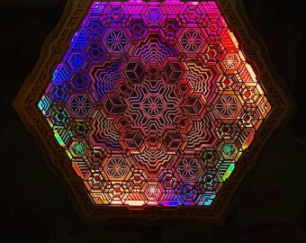Può includere: Un apparecchio di illuminazione esagonale geometrico con intricati motivi a strati. L'apparecchio è illuminato con una vibrante gamma di colori, tra cui rosso, blu, viola e verde. Il testo "with addressable smart LED strip" è visibile in basso.
