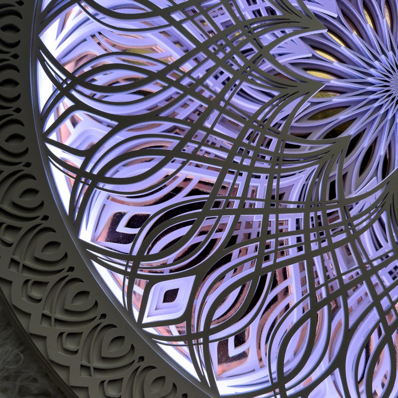 May include: A circular wall art piece featuring multiple layered cutouts with intricate, symmetrical, petal-like patterns. The layers are illuminated from behind with a soft purple light, casting shadows and highlighting the depth of the design.