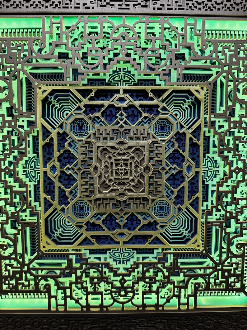 Pu&ograve; includere: Un'opera d'arte geometrica a strati con intricati motivi ritagliati. Il design presenta un quadrato centrale con un design simmetrico complesso in oro, blu e grigio, circondato da strati di forme verdi e marrone scuro. L'effetto complessivo &egrave; un'opera d'arte dettagliata e tridimensionale.