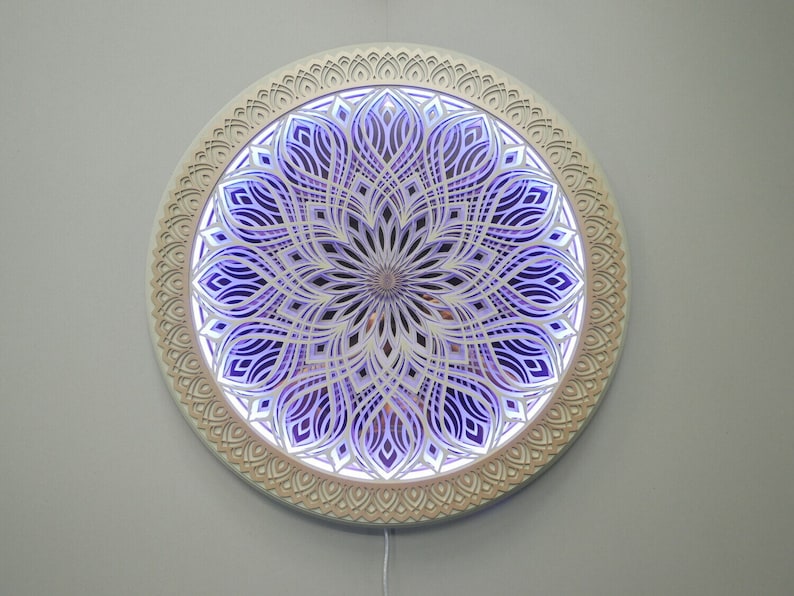 May include: A circular wall-mounted light fixture featuring intricate, layered, laser-cut wooden panels arranged in a symmetrical mandala pattern. The design displays a series of concentric, petal-like cutouts illuminated from behind by a vibrant purple glow.