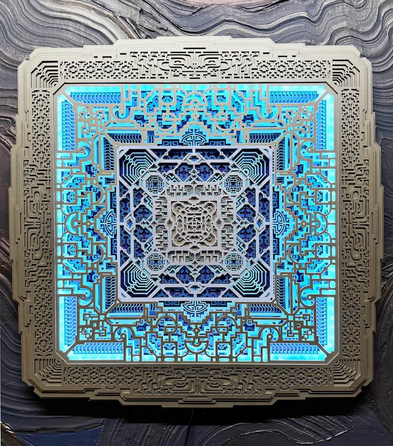 Pu&ograve; includere: Un'opera d'arte murale quadrata a strati con intricati motivi geometrici. L'opera presenta una cornice grigio chiaro e un design centrale nei toni del blu e del bianco, illuminato da una morbida luce blu. Il design ha un effetto a strati, creando profondit&agrave;.
