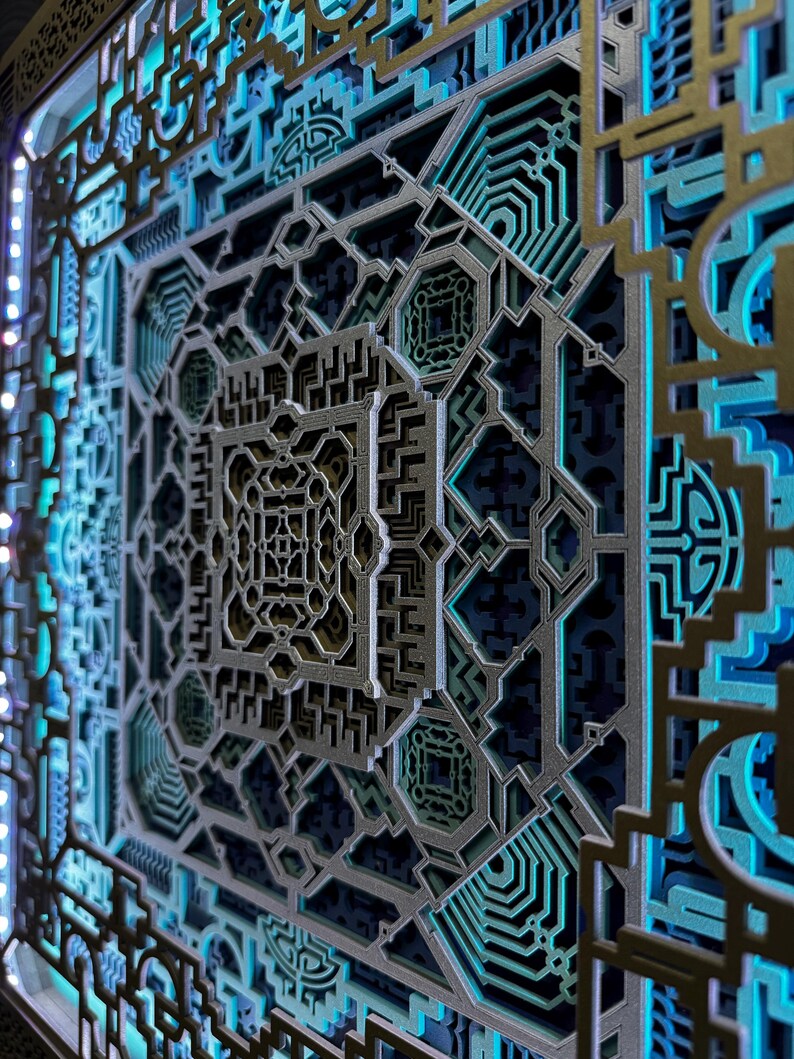 Pu&ograve; includere: Un'opera d'arte murale geometrica a strati con motivi intricati. Il design presenta forme tagliate al laser in tonalit&agrave; argento, oro e verde acqua, creando un effetto 3D. L'opera d'arte &egrave; illuminata da luci a LED blu, che ne esaltano la profondit&agrave; e i dettagli.