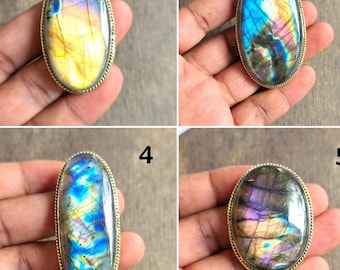 May include: Nine oval and teardrop-shaped labradorite gemstone cabochons with iridescent colors of blue, yellow, purple, and green. Each stone is set in a gold-colored metal bezel, displayed on a hand.