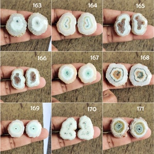 May include: Nine pairs of agate slices with different patterns and colors, including white, brown, green, and pink. The agate slices are arranged in a grid pattern on a wooden surface.