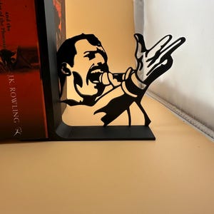K&ouml;nnte beinhalten: Schwarzer Metall-Buchst&uuml;tze mit der Silhouette eines S&auml;ngers mit Mikrofon und ausgestreckter Hand. Diese dekorative Buchst&uuml;tze ist f&uuml;r das Aufrechtstellen von B&uuml;chern gedacht. Das Design ist eine Hommage an einen ber&uuml;hmten S&auml;nger und verleiht jedem B&uuml;cherregal eine besondere Note.