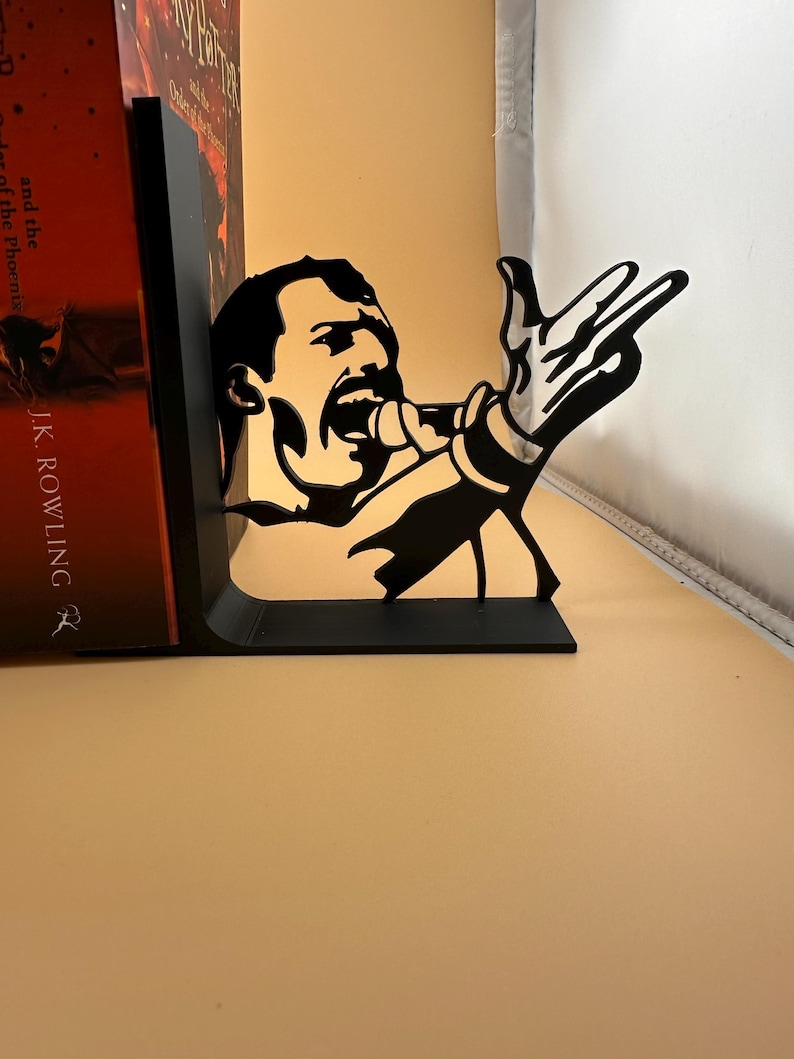 K&ouml;nnte beinhalten: Schwarzer Metall-Buchst&uuml;tze mit der Silhouette eines S&auml;ngers mit Mikrofon und ausgestreckter Hand. Diese dekorative Buchst&uuml;tze ist f&uuml;r das Aufrechtstellen von B&uuml;chern gedacht. Das Design ist eine Hommage an einen ber&uuml;hmten S&auml;nger und verleiht jedem B&uuml;cherregal eine besondere Note.